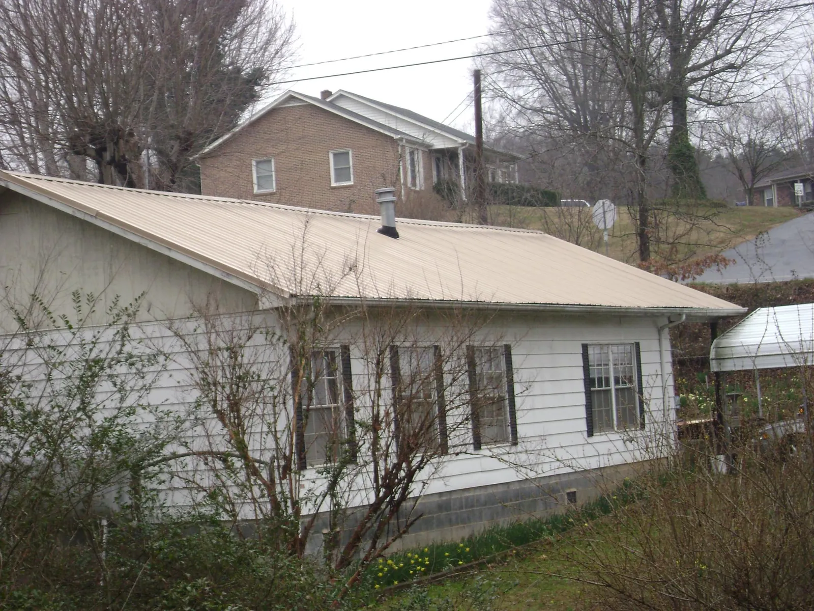 Tan metal roof on a white sided house set into a hillside — Commercial Roofing by Roofing Brothers in Abingdon